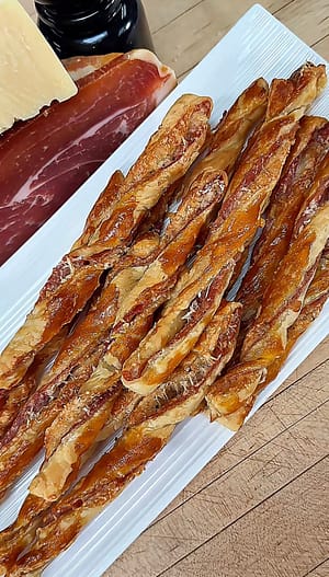Puff Pastry Grissini layered with Prosciutto di Parma and Parmigiano Reggiano, baked until flaky, crisp, and golden brown.