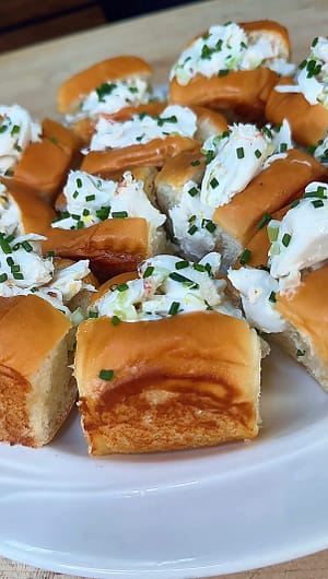 Mini Crab Rolls filled with fresh lump crabmeat, lemon, chives, and celery served on buttery toasted rolls.