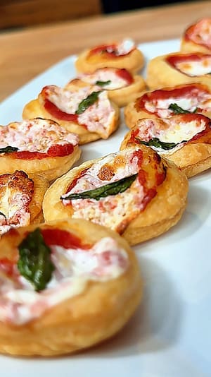 Pizzette di Sfoglia topped with tomato sauce, mozzarella, basil, and flaky golden puff pastry.